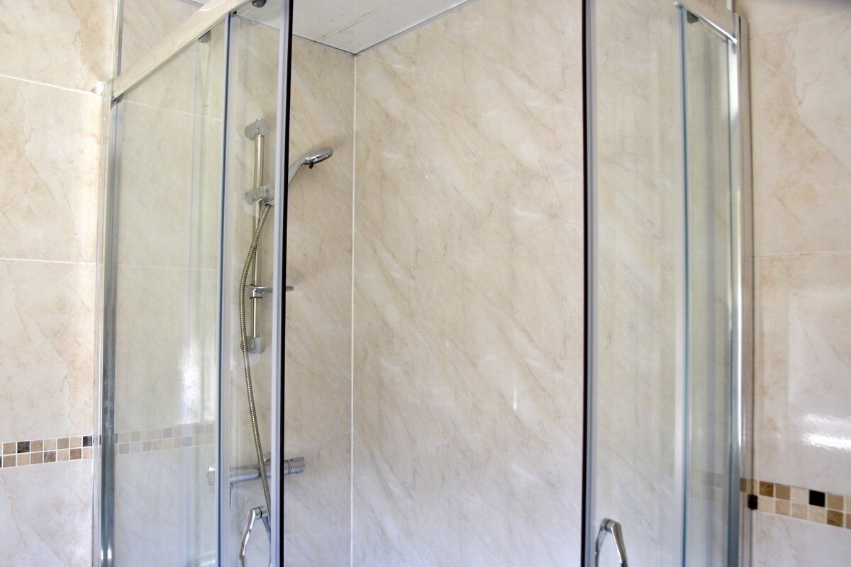 Une douche fermée par des parois en verre, dotée d’un pommeau de douche à main et d’un robinet mural.