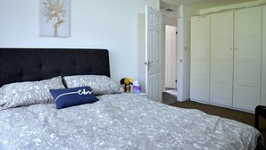 A bedroom with a bed, a nightstand, a vase with flowers, and a door leading to another room.
