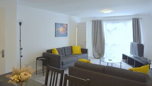 A modern living room with a grey sofa, a small round coffee table, and a TV on a stand.