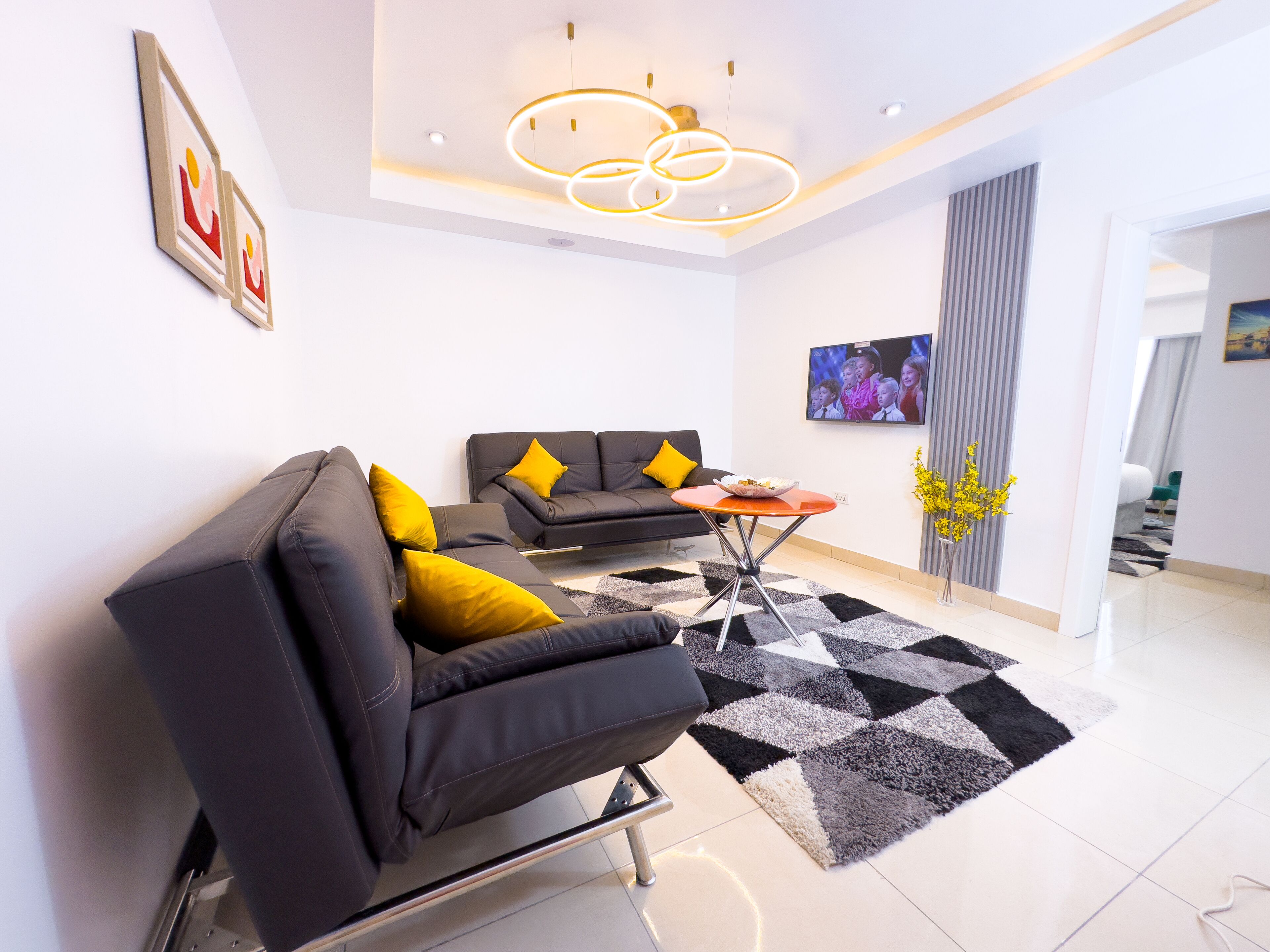Una sala de estar moderna con un sofá negro, un sofá más pequeño con cojines amarillos, una mesita de centro y una alfombra blanco y negro.