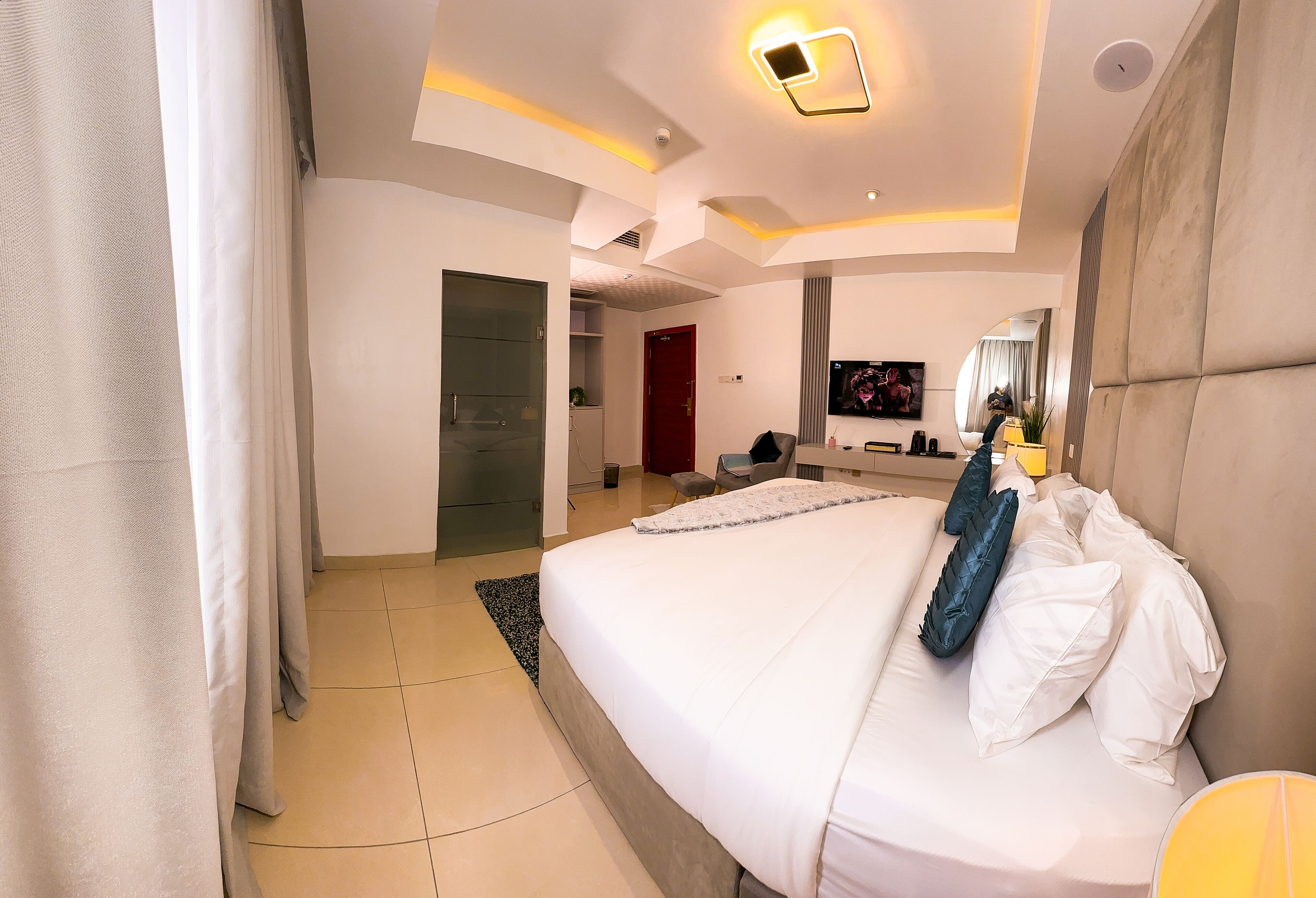 Une chambre d’hôtel moderne avec un grand lit, une télévision et une salle de bain visible au fond.