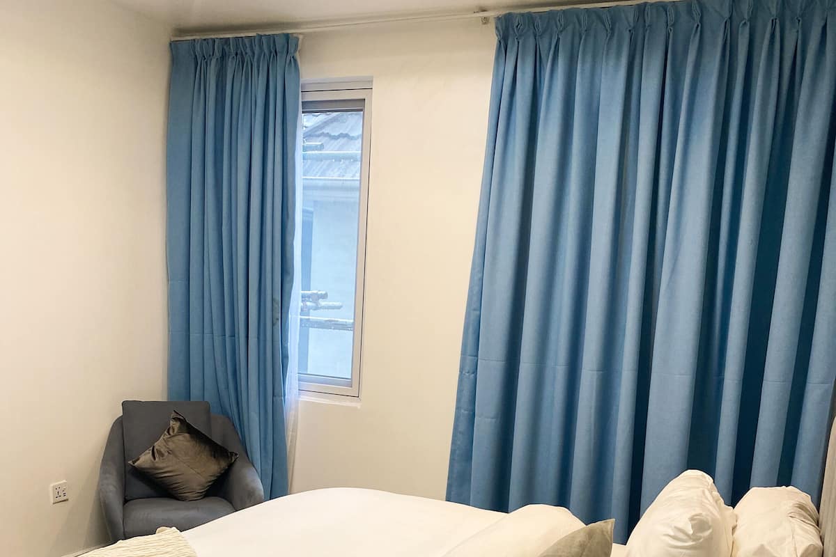 A bedroom with a bed, pillows, a chair, and curtains.