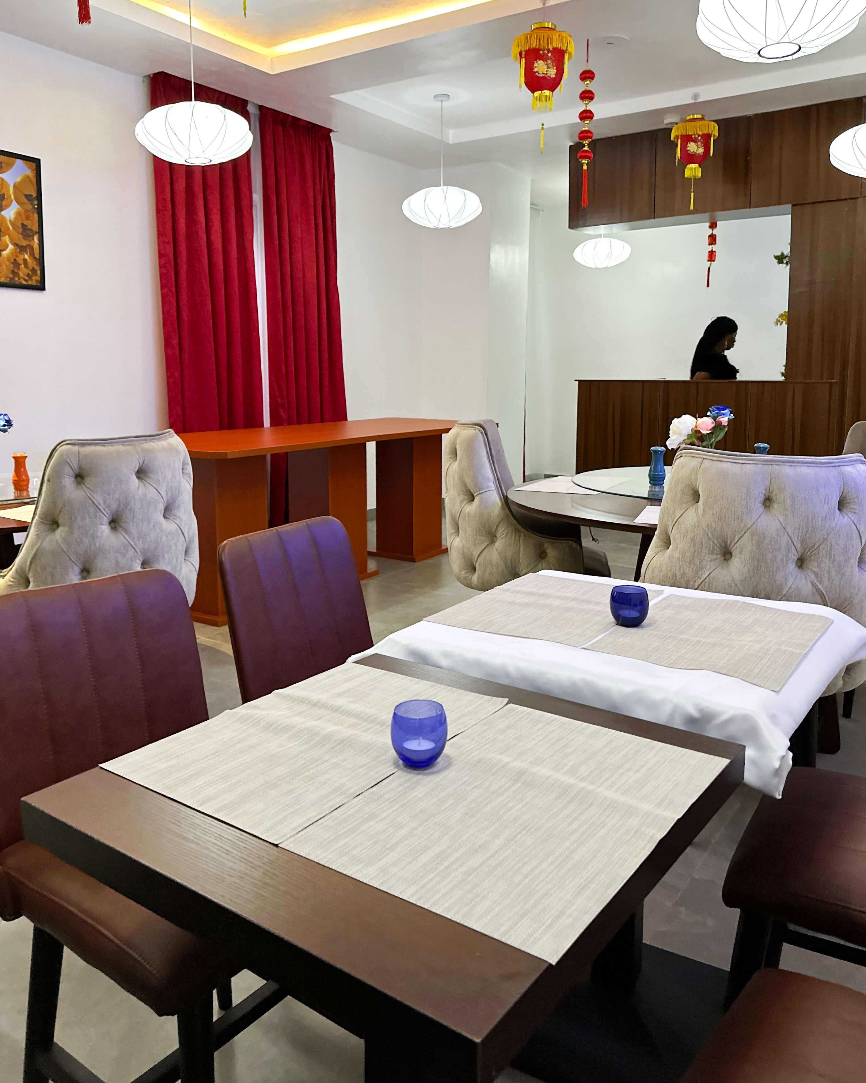 A hotel dining area with tables and chairs, red curtains, and hanging lanterns.