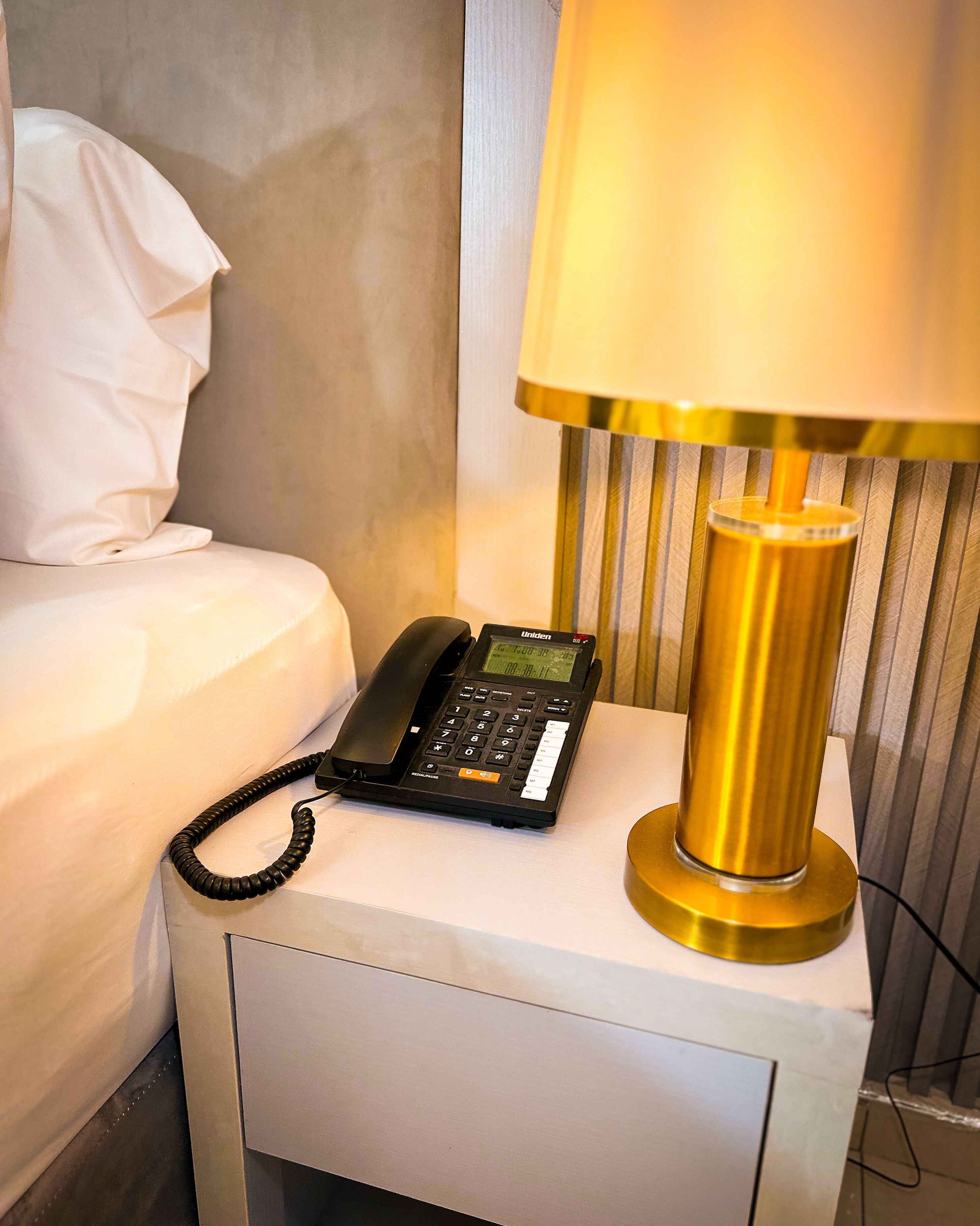 A hotel room with a bed, a bedside table, a lamp, and a phone.
