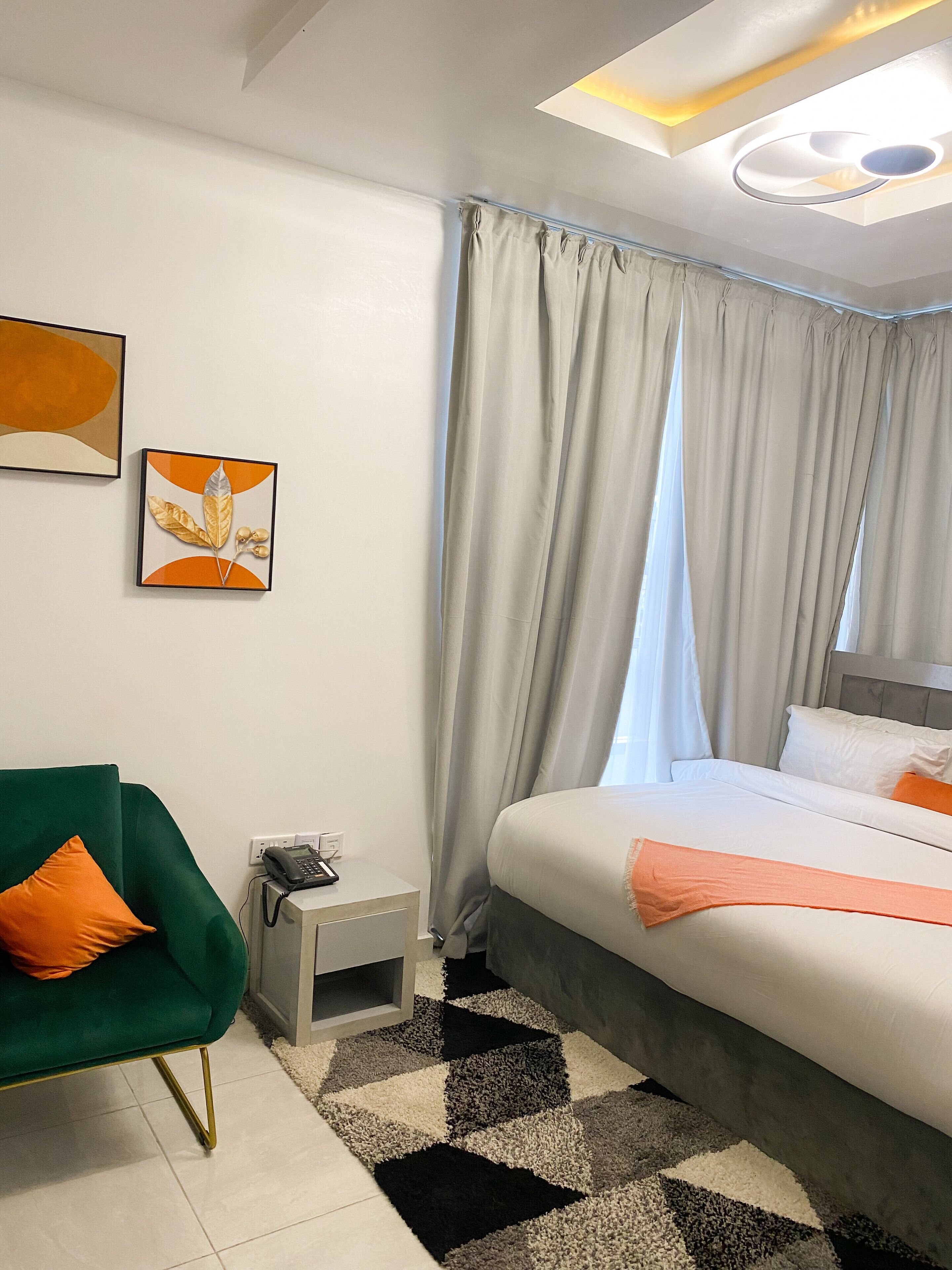 Ein modernes Hotelzimmer mit Bett, einem grünen Sessel, einem kleinen Nachttisch und einem an der Wand befestigten Telefon.