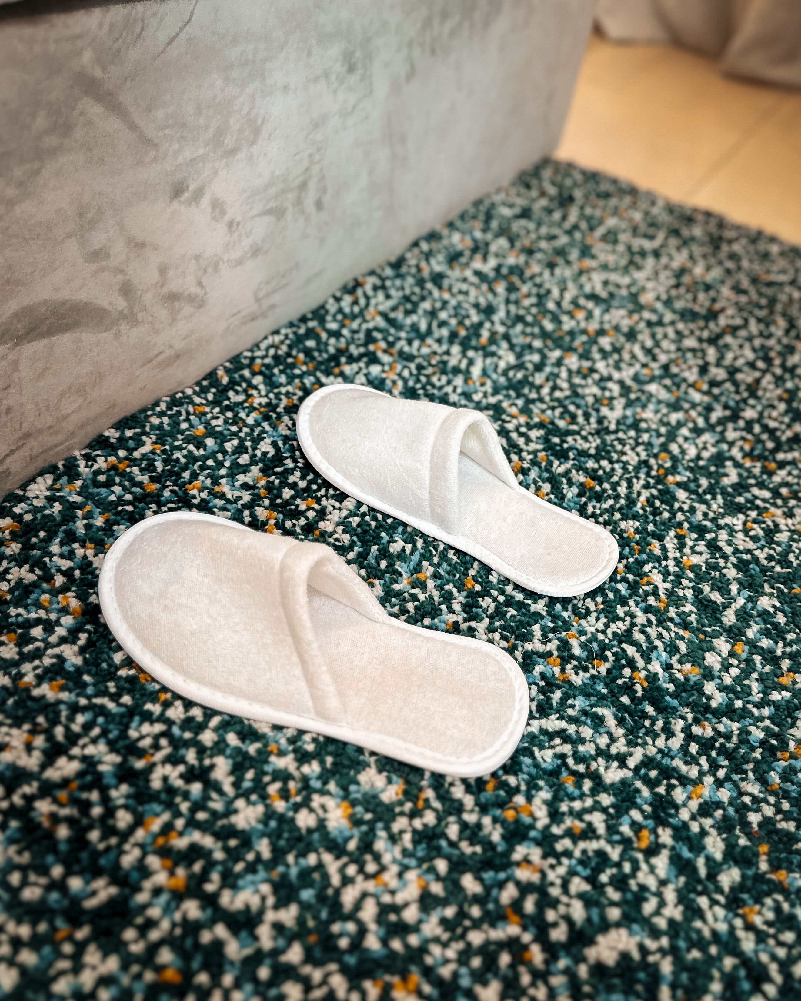 Une paire de pantoufles blanches sur un tapis vert et blanc à motifs.