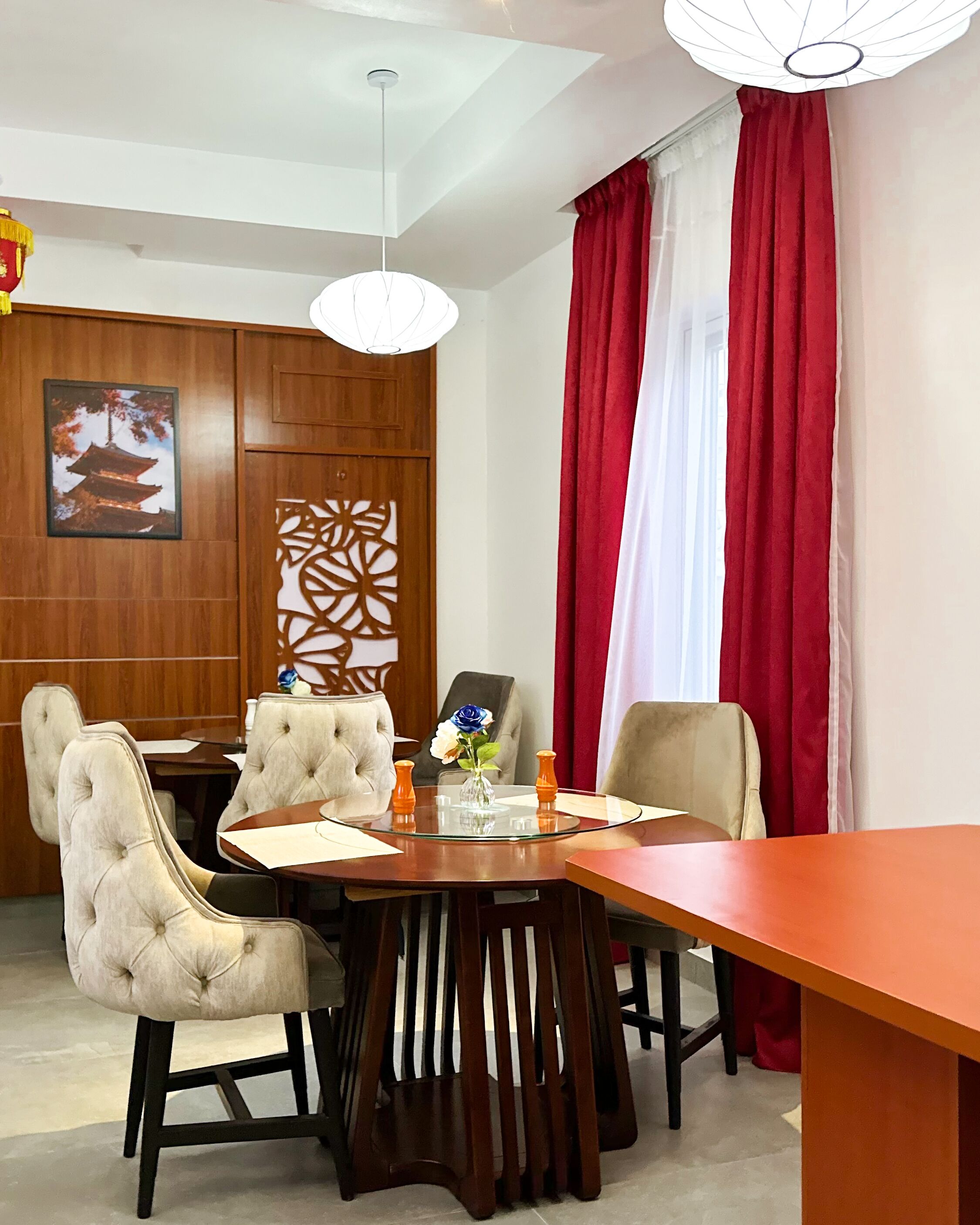 A dining area with a round table, four upholstered chairs, a vase with flowers, and a decorative panel on the wall.