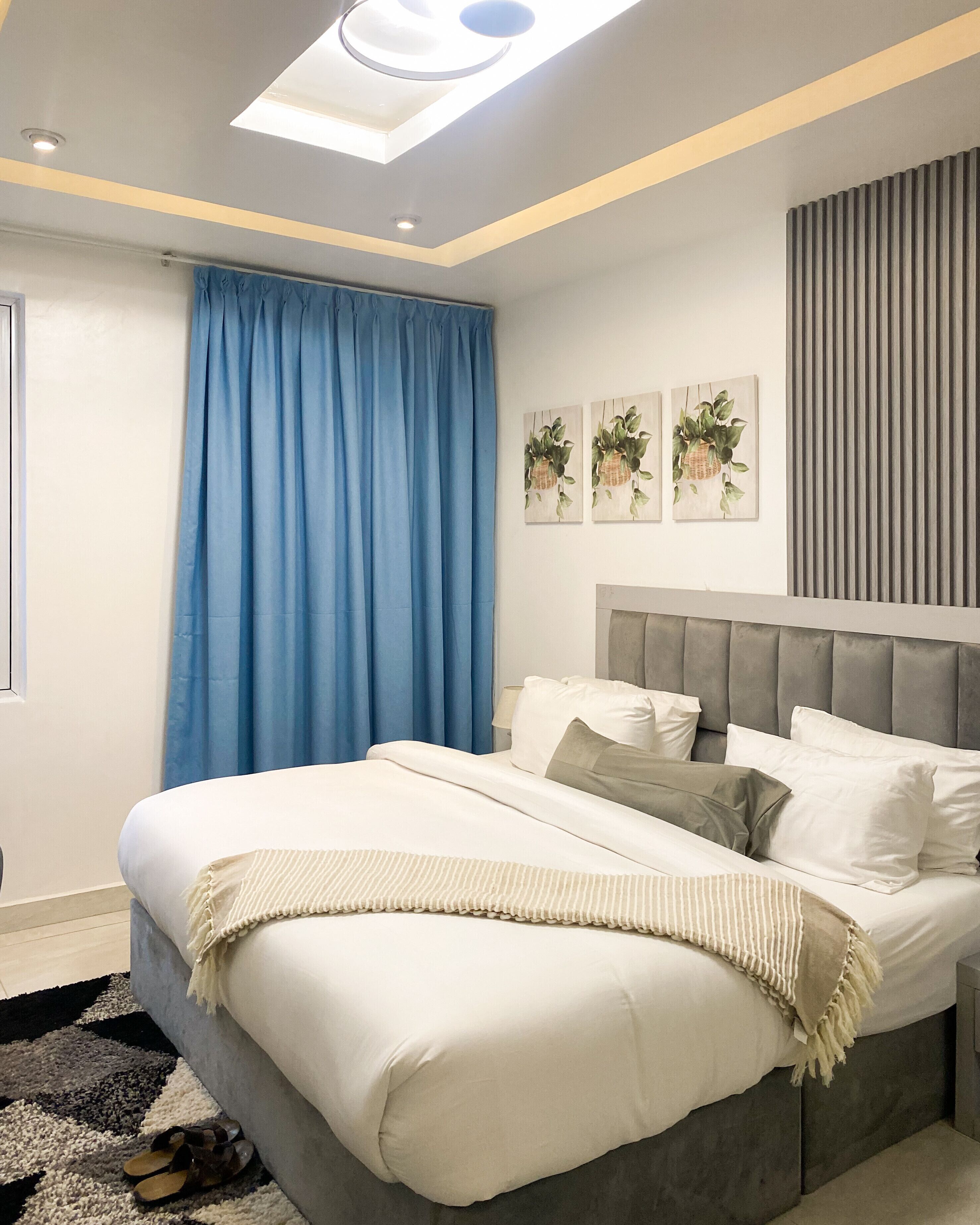 A modern bedroom with a large bed, a skylight, a blue curtain, and wall-mounted artwork.
