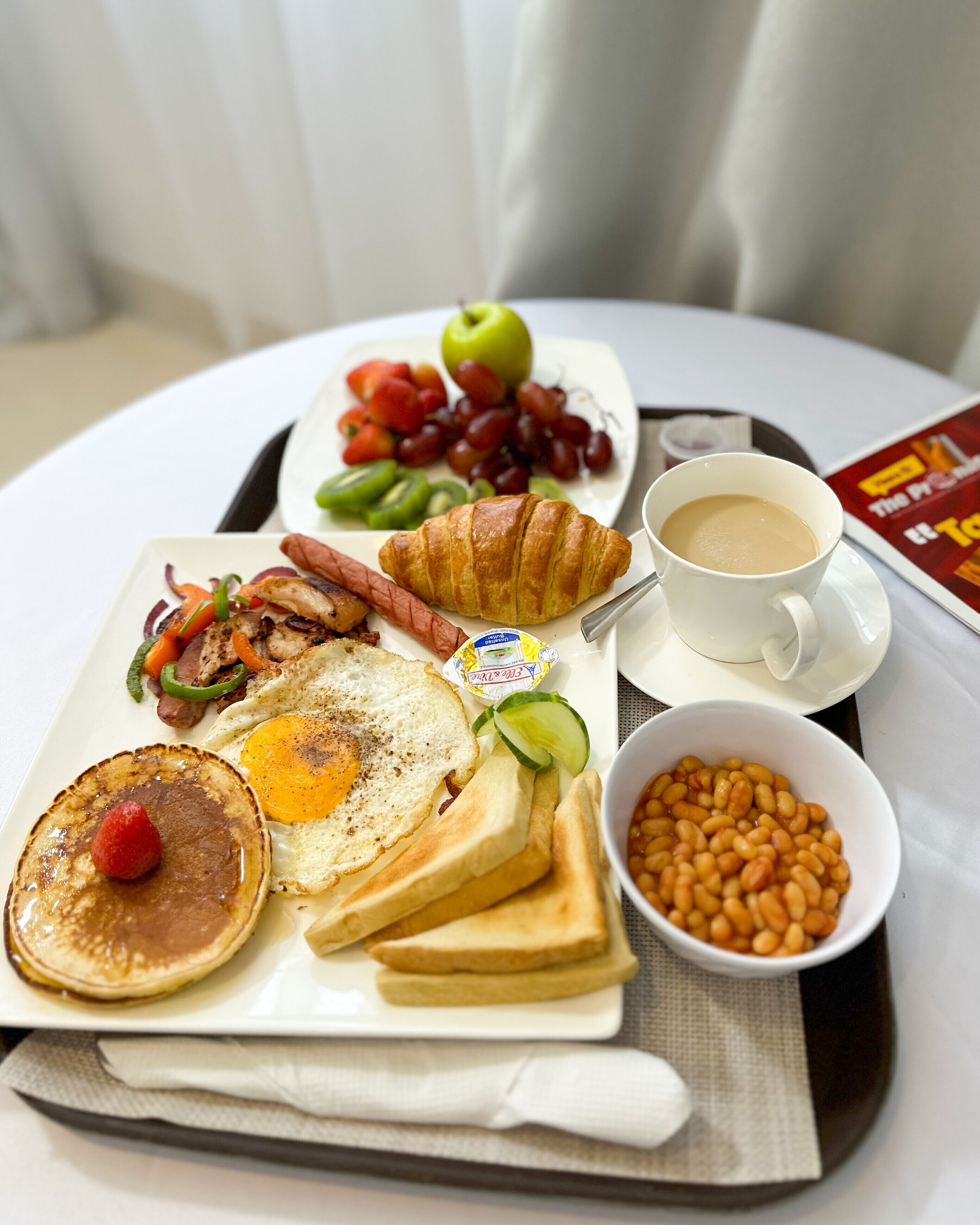 A tray with breakfast items including eggs, toast, pancakes, a croissant, and a cup of coffee.