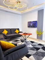 A modern living room with a black sofa, yellow cushions, a round coffee table, and a black-and-white patterned rug.