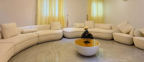 A modern living room with a curved sectional sofa, a central coffee table, and a decorative chandelier.