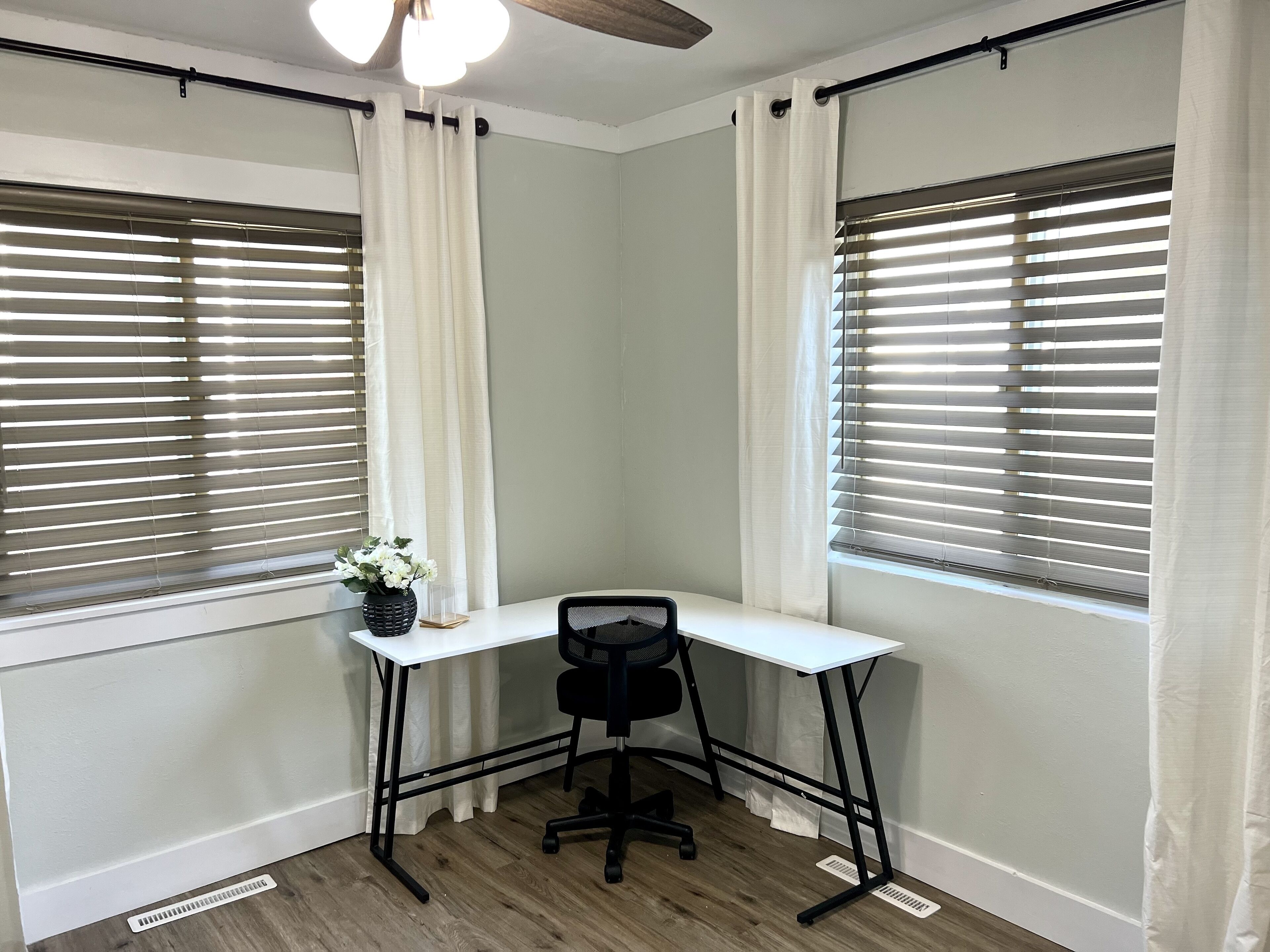 A corner office with a white desk, black office chair, and a small potted plant.
