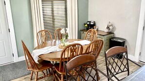 A dining area with a round table, wooden chairs, a ceiling fan, and a window with blinds.