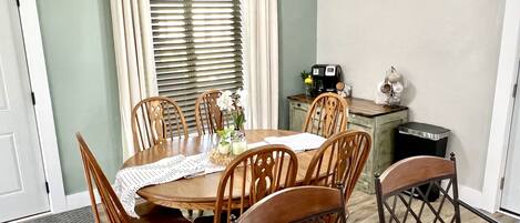 A dining area with a round table, wooden chairs, a ceiling fan, and a window with blinds.