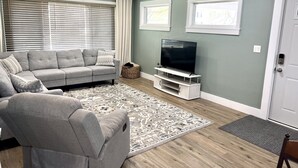A living room with a grey sofa, a television on a white stand, a patterned rug, and a door with a keypad lock.