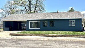 A single-story house with a dark blue exterior, a covered garage, and a well-maintained lawn.
