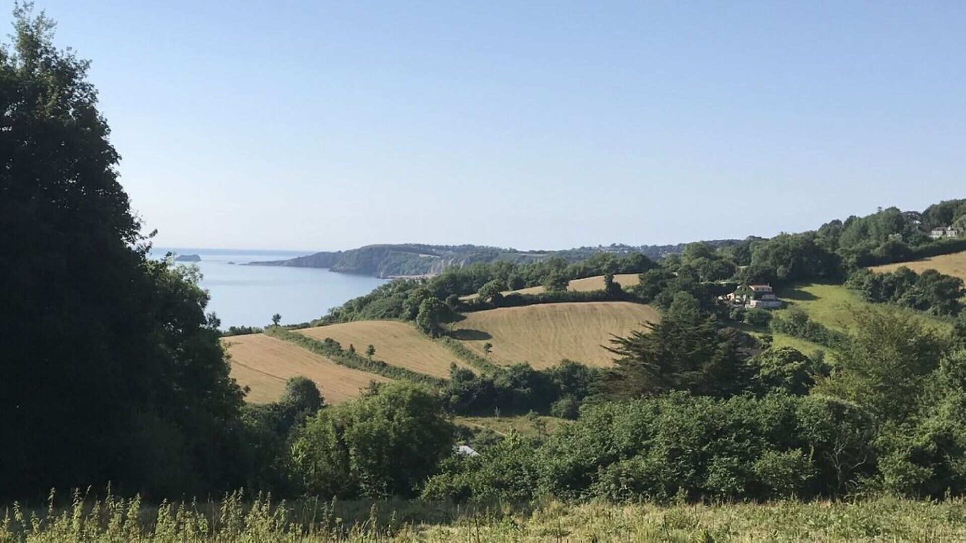 Un paysage côtier caractérisé par des collines douces, des champs et une étendue d’eau.