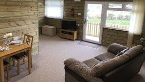 A cozy cabin interior with a wooden dining table, a sofa, a television, and a sliding glass door leading to a deck. - Coastal retreat Converted Stables, ,  close to Maidencombe beach & pubs. (Stokeinteignhead Torquay,)
