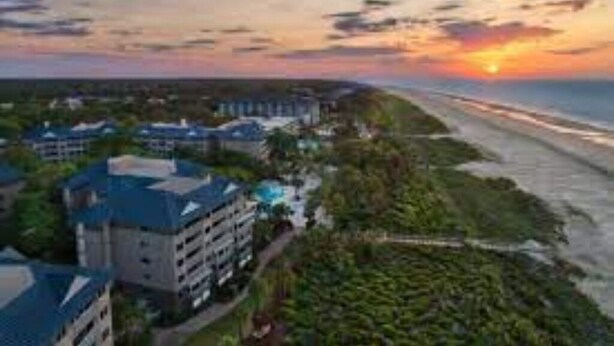 Ein Hotel an der Küste mit mehreren Gebäuden, einem Strand und einem Sonnenuntergang.