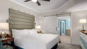 Ein Hotelzimmer mit Bett, Nachttischen, einem Sessel und einem Deckenventilator, mit Blick auf den Flur.