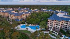 Ein Resort mit mehreren Gebäuden, einem zentralen Poolbereich und umliegender Bepflanzung.