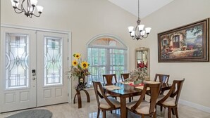 Une salle à manger avec une table et des chaises en bois, un lustre et un tableau au mur.