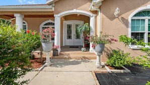 Une maison à l’extérieur beige, avec des colonnes blanches et une véranda couverte ornée de plantes en pot.