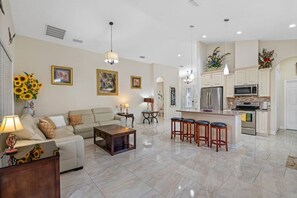 Amplia sala de estar con sofá, mesa de centro y taburetes de bar. Cocina equipada con refrigerador, microondas y estufa.
