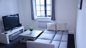 A modern living room with a grey sofa, a flat-screen TV, a coffee table, and a potted plant. - Captivating 1-bed Apartment in Nottingham (Nottingham)