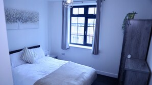 A neatly arranged bedroom with a bed, a window with curtains, a bedside table, and a wardrobe. - Captivating 1-bed Apartment in Nottingham (Nottingham)