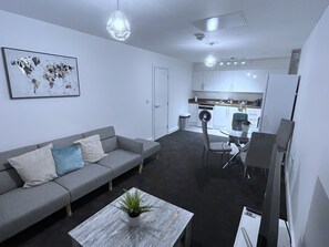 A modern living room with a grey sofa, a coffee table with a plant, and a dining area with a glass table and chairs. - Captivating 1-bed Apartment in Nottingham (Nottingham)