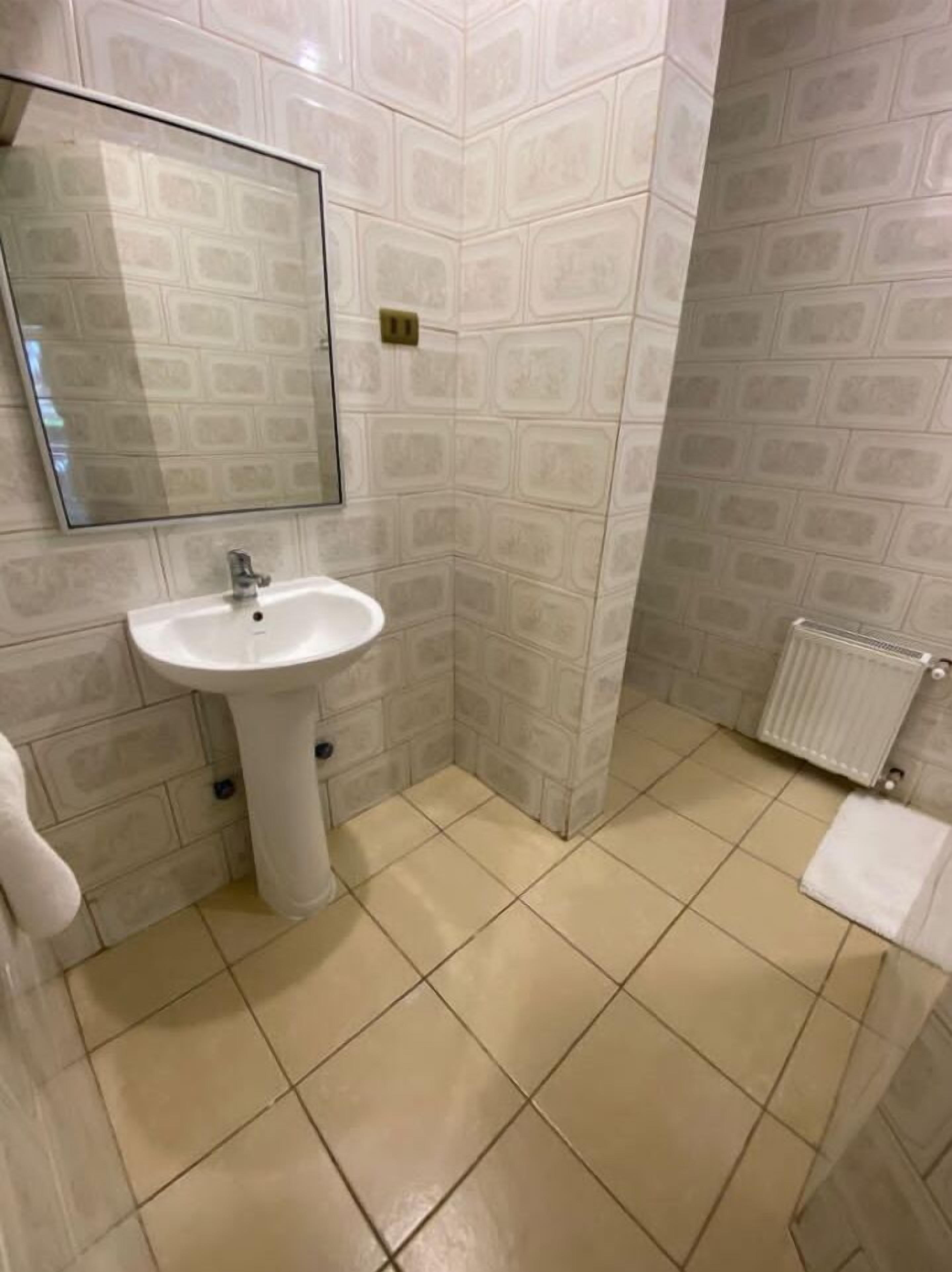 Un baño con un lavamanos pedestal blanco, un espejo encima y un radiador en la pared.
