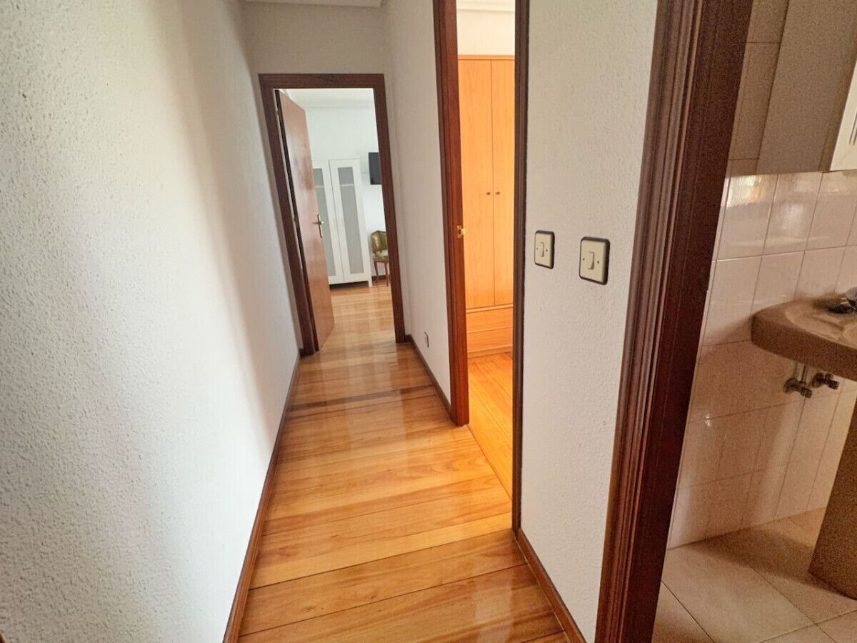 A narrow hallway with wooden flooring and white walls.
