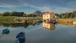 Ein ruhiger See mit Booten, ein Steinhaus mit rotem Dach und eine Hügelkette im Hintergrund.