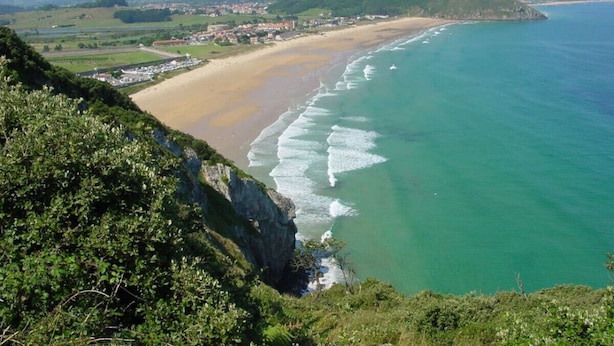 Eine Küstenlandschaft mit Strand, Meer und Hügeln im Hintergrund.