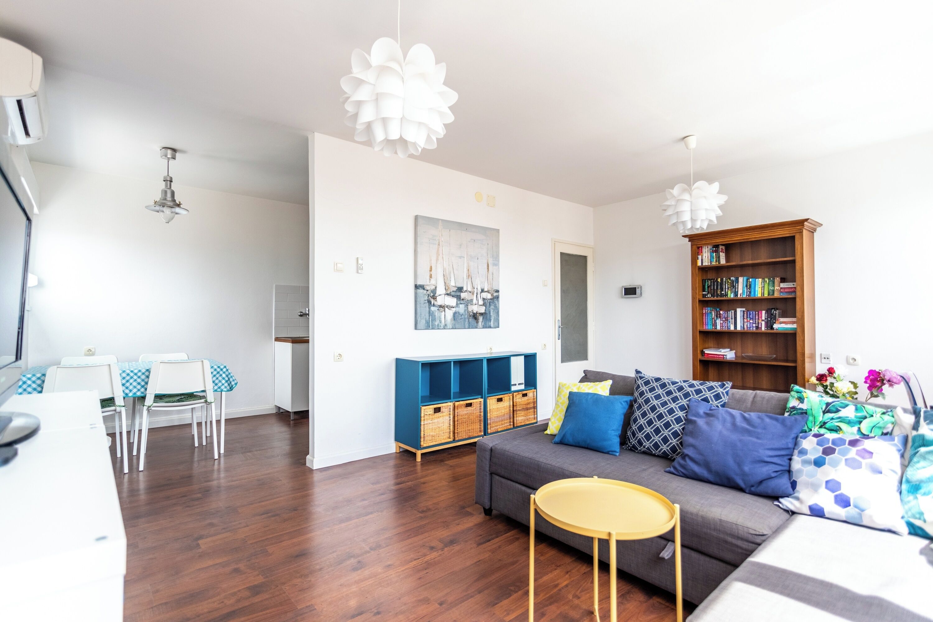 Ein Wohnzimmer mit einer Couch, einem kleinen runden Tisch, einem Bücherregal und einem Essbereich mit Stühlen und Tisch.