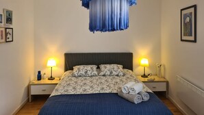 Ein ordentlich bezogenes Bett mit Blumenmuster, zwei Nachttischlampen und einer blau-weiß gestreiften Tagesdecke.