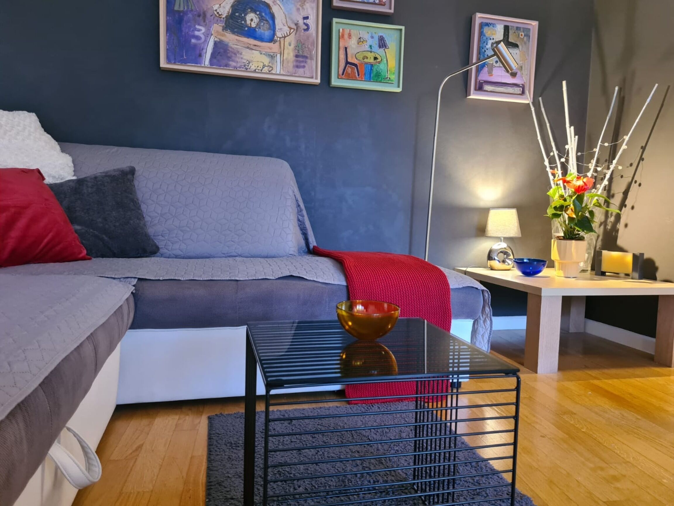 A modern living room with a grey sofa, a black coffee table, and a small side table with a lamp and a vase of flowers.