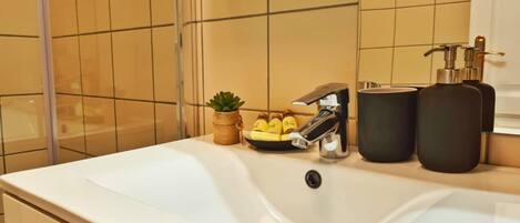 A bathroom with a white sink, a small potted plant, a soap dispenser, and a bottle of shampoo.