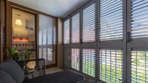 Ein modernes Zimmer mit einer Couch, einem kleinen runden Tisch und Blick durch ein Fenster mit Jalousien.