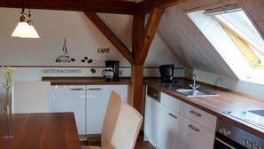 Cocina compacta con muebles blancos, una mesa de comedor de madera y un tragaluz.