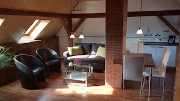 Una sala de estar acogedora con un sofá, dos sillones, una mesa de centro de vidrio y un comedor con mesa y sillas.