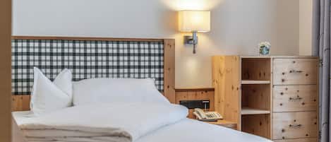 Quarto de hotel com cama, mesa de cabeceira com abajur, telefone e armário de madeira com gavetas.