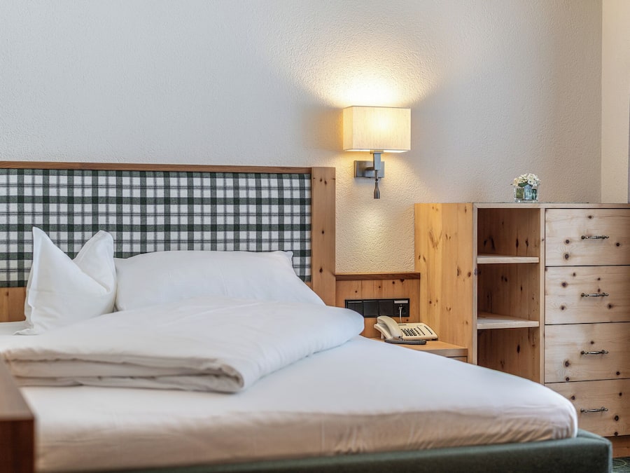 A hotel room with a bed, a bedside table with a lamp, a telephone, and a wooden cabinet with drawers.