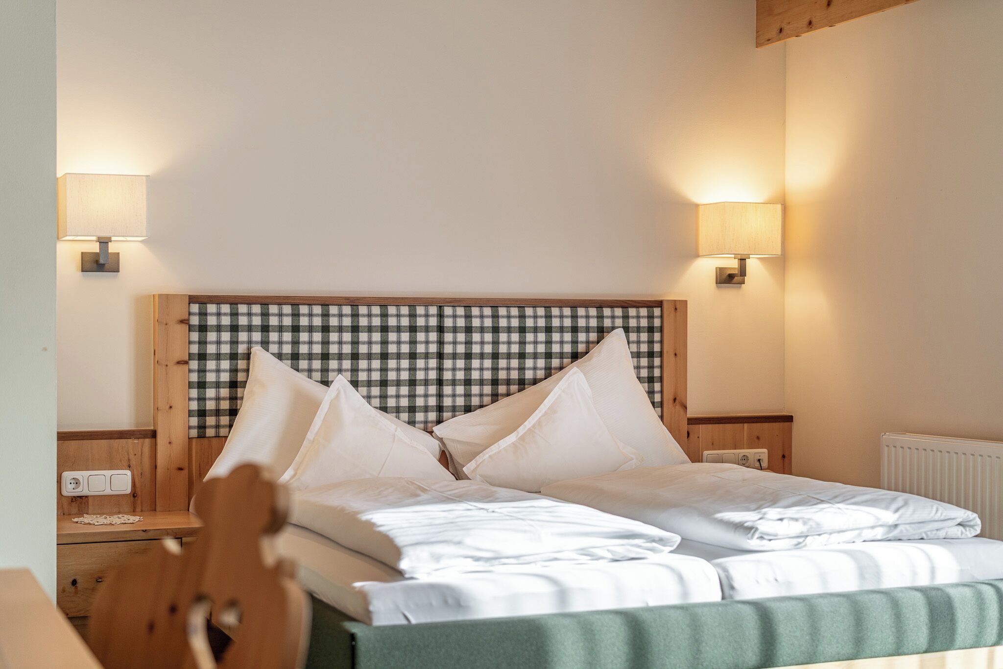 A neatly made bed with a plaid headboard, two bedside lamps, and a wooden nightstand with a lamp.