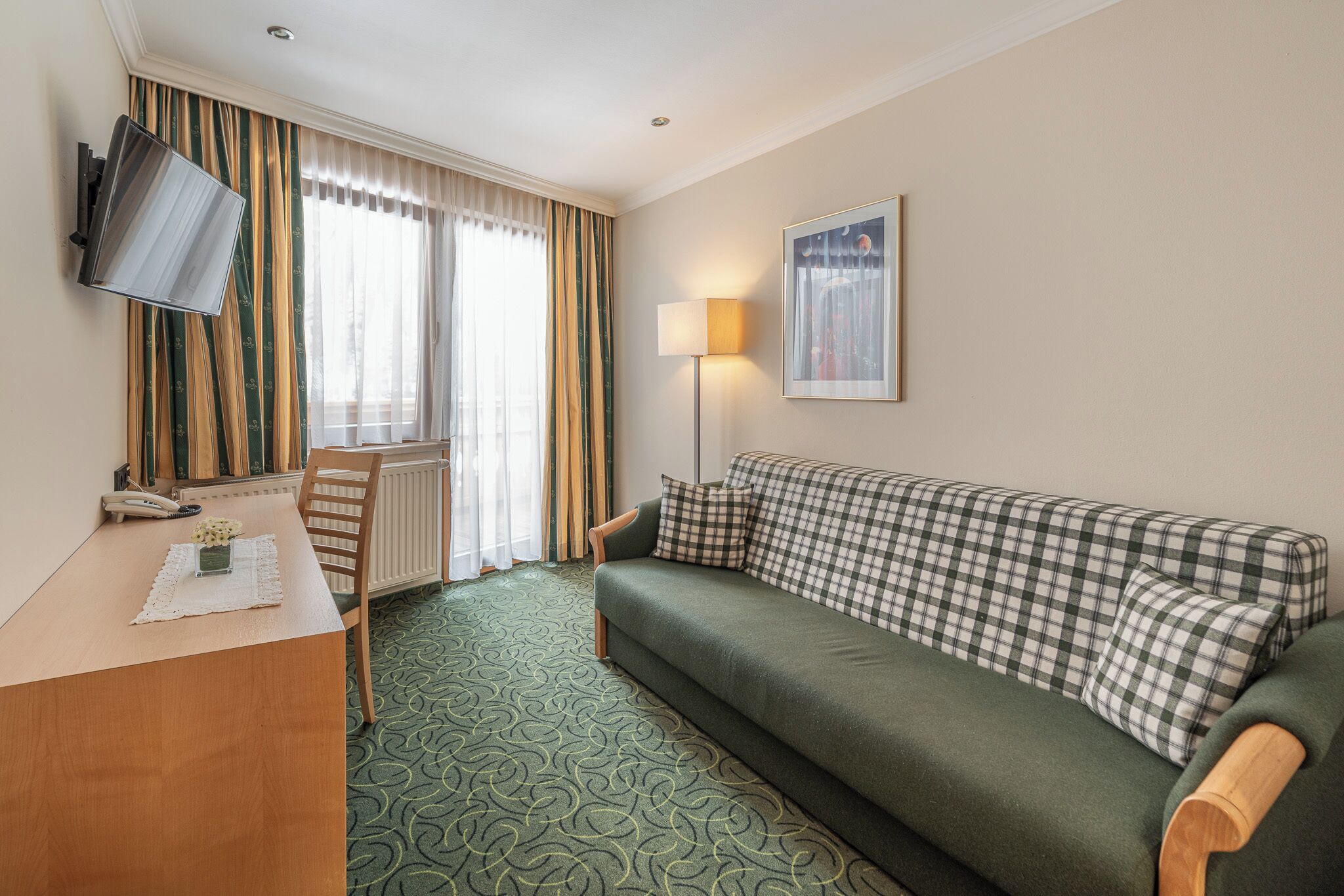Ein Hotelzimmer mit einem grünen Sofa, einem Holztisch, einem Fernseher, einer Lampe und einem Fenster mit Vorhängen.