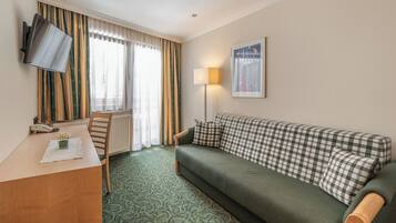 Ein Hotelzimmer mit einem grünen Sofa, einem Holztisch, einem Fernseher, einer Lampe und einem Fenster mit Vorhängen.