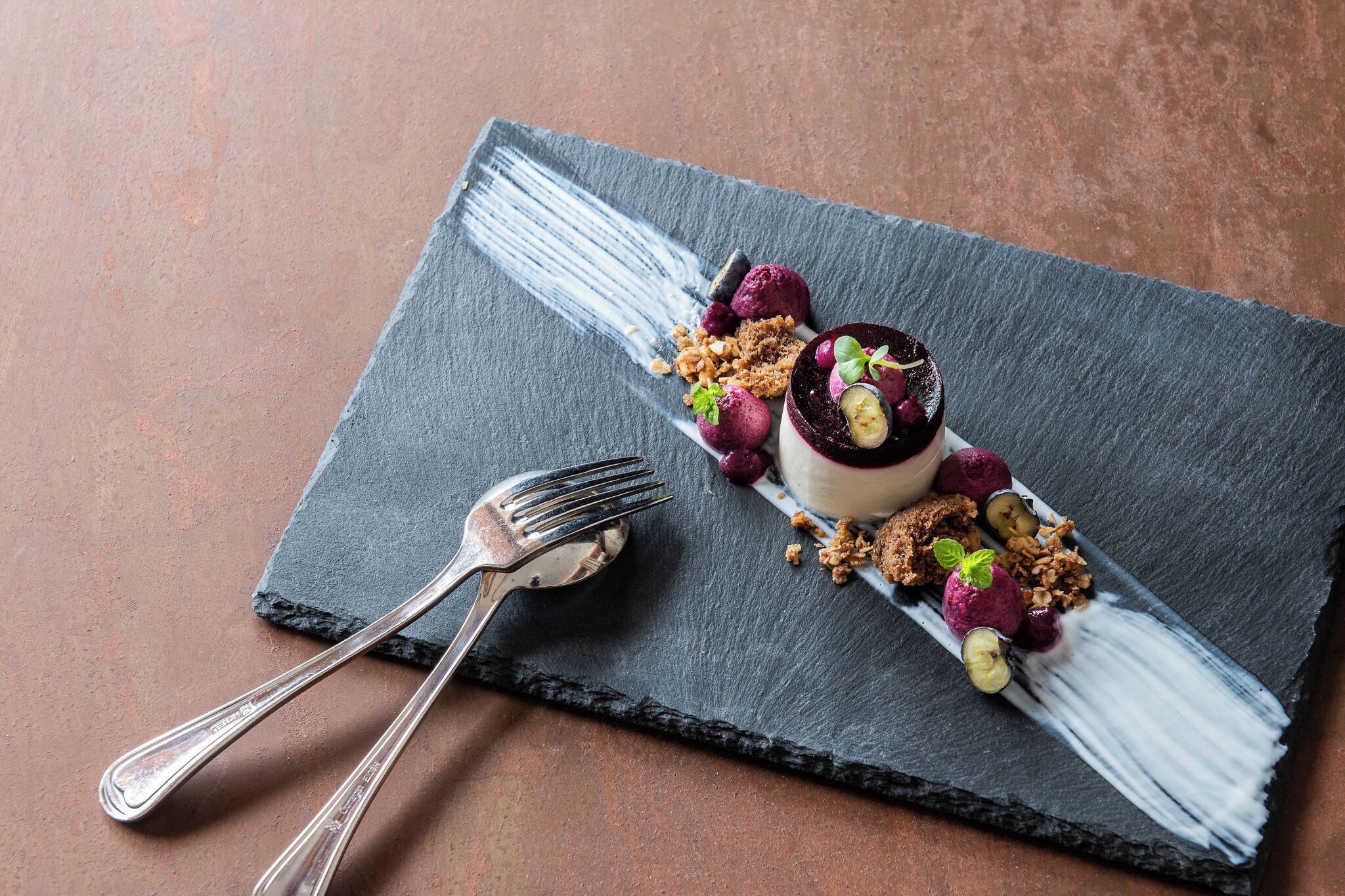 A dessert on a slate plate with a fork and spoon beside it.