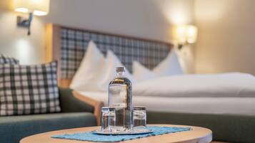 A hotel room with a bed, a round table with a clear bottle and glasses, and a checkered pillow.