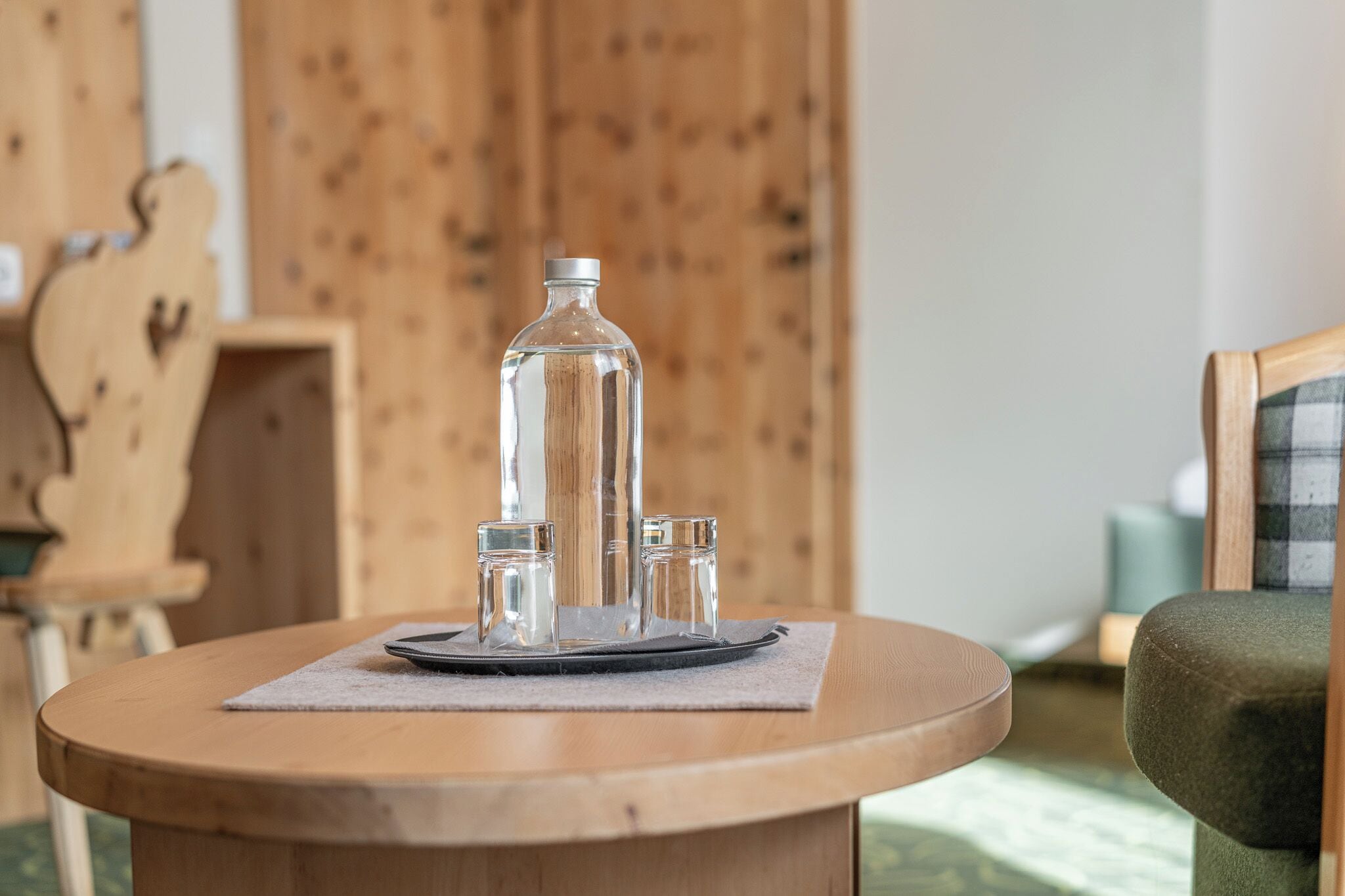 Une table ronde en bois, une bouteille en verre transparent, deux petits verres et un plateau en métal.